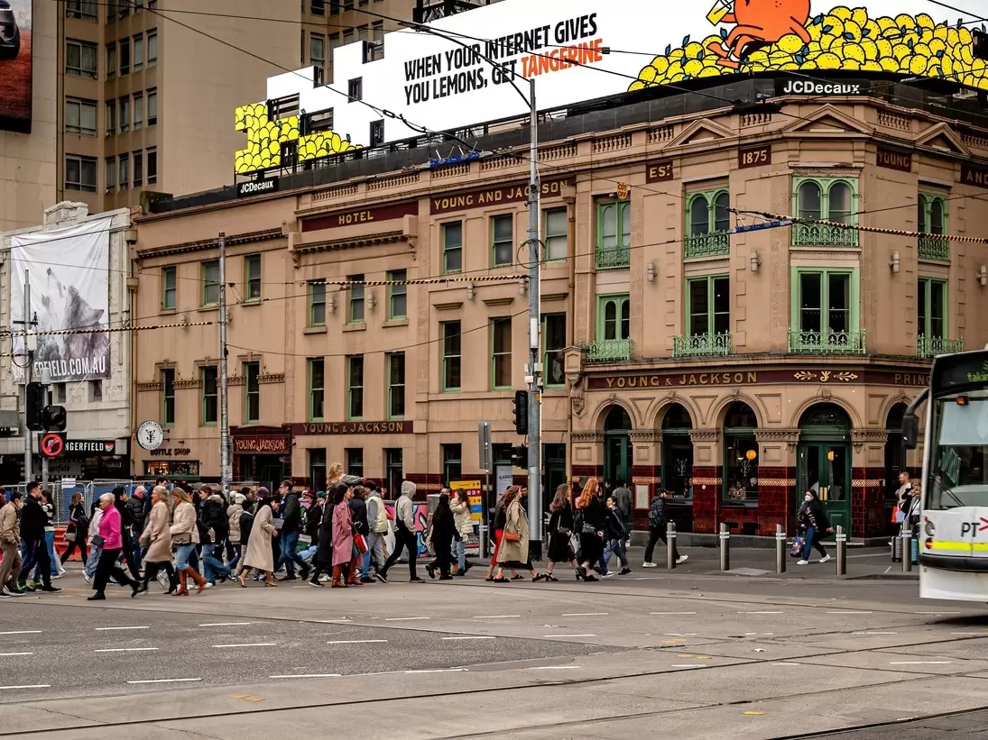Pedestrians crossing the intersection of Flinders St and Swanston St with historic Young and Jackson's pub on the corner. Melbourne, Australia.