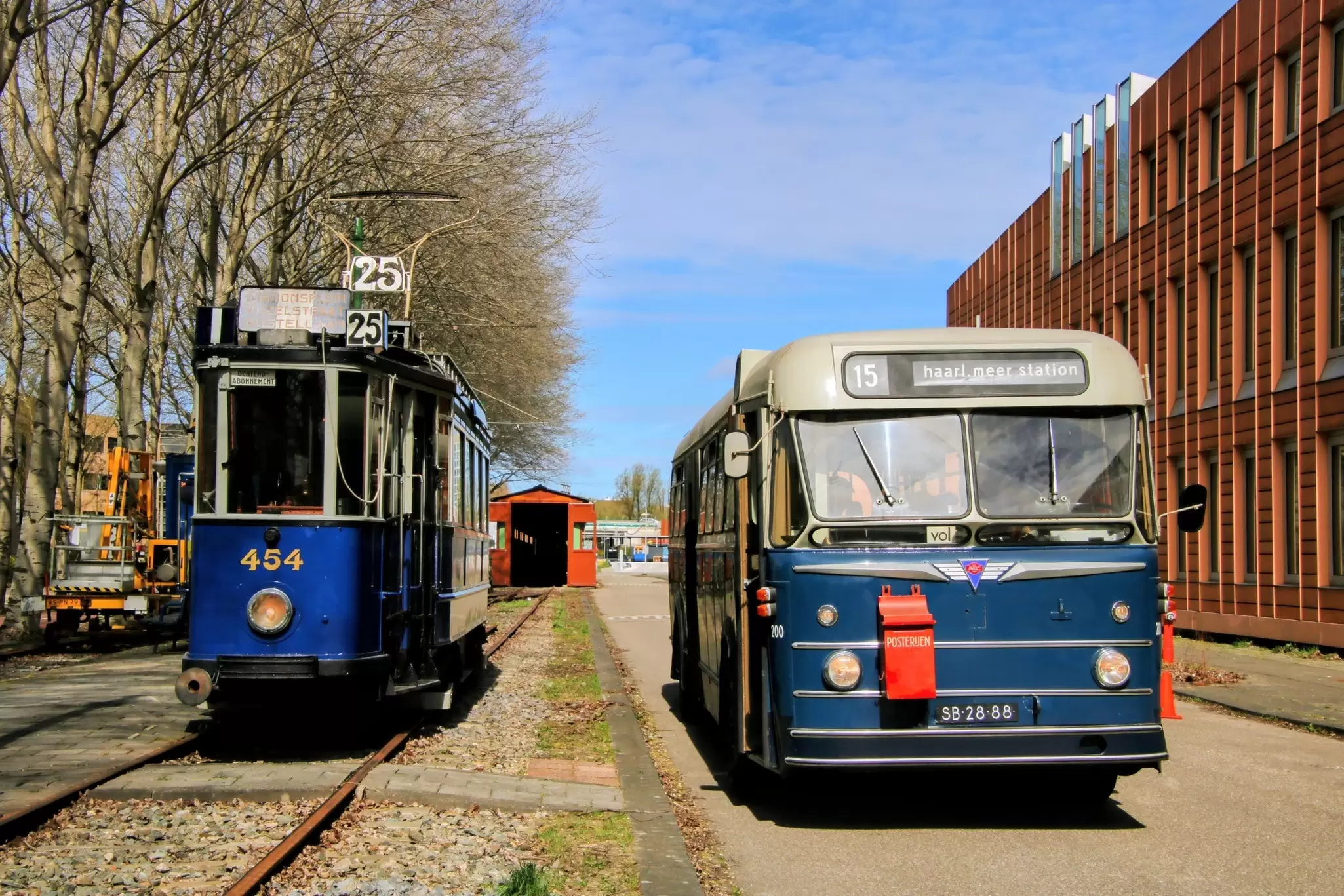 View of a historic blue tram and bus of the Electrische Museumtramlijn Amsterdam on a sunny day.