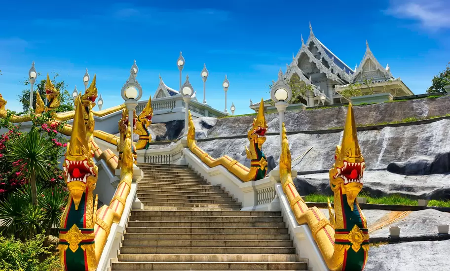 Stone staircase flanked by golden naga serpent statues at a white Thai Buddhist temple