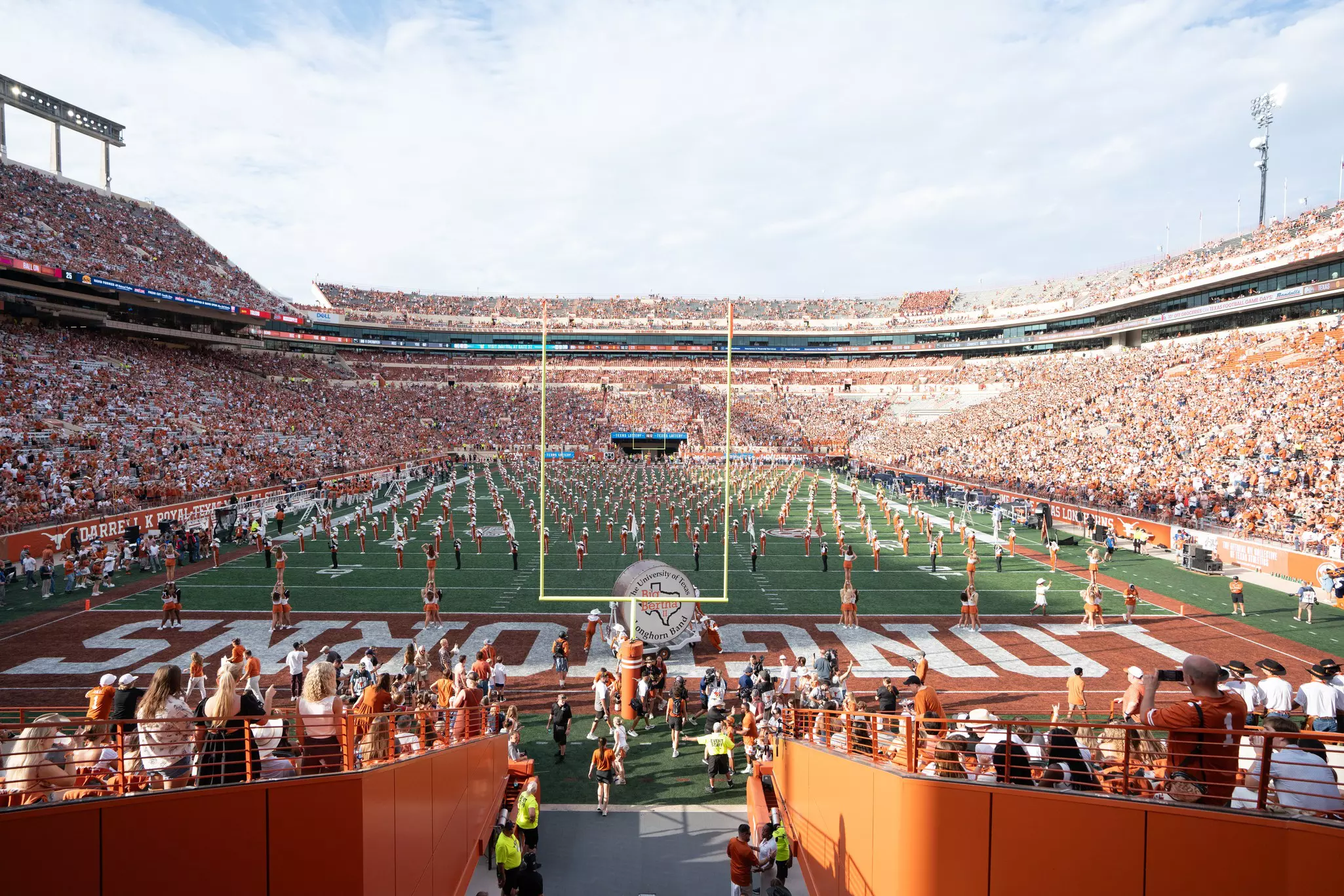 A football stadium on game day is pictured, with a marching band on the field and tens of thousands of spectators in the bleachers.