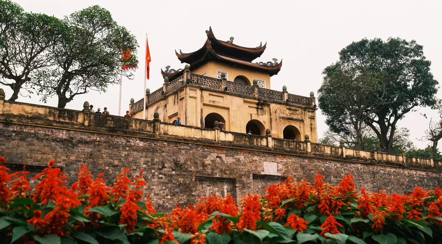 The Thang Long Citadel in Hanoi with red flowers in the foreground.