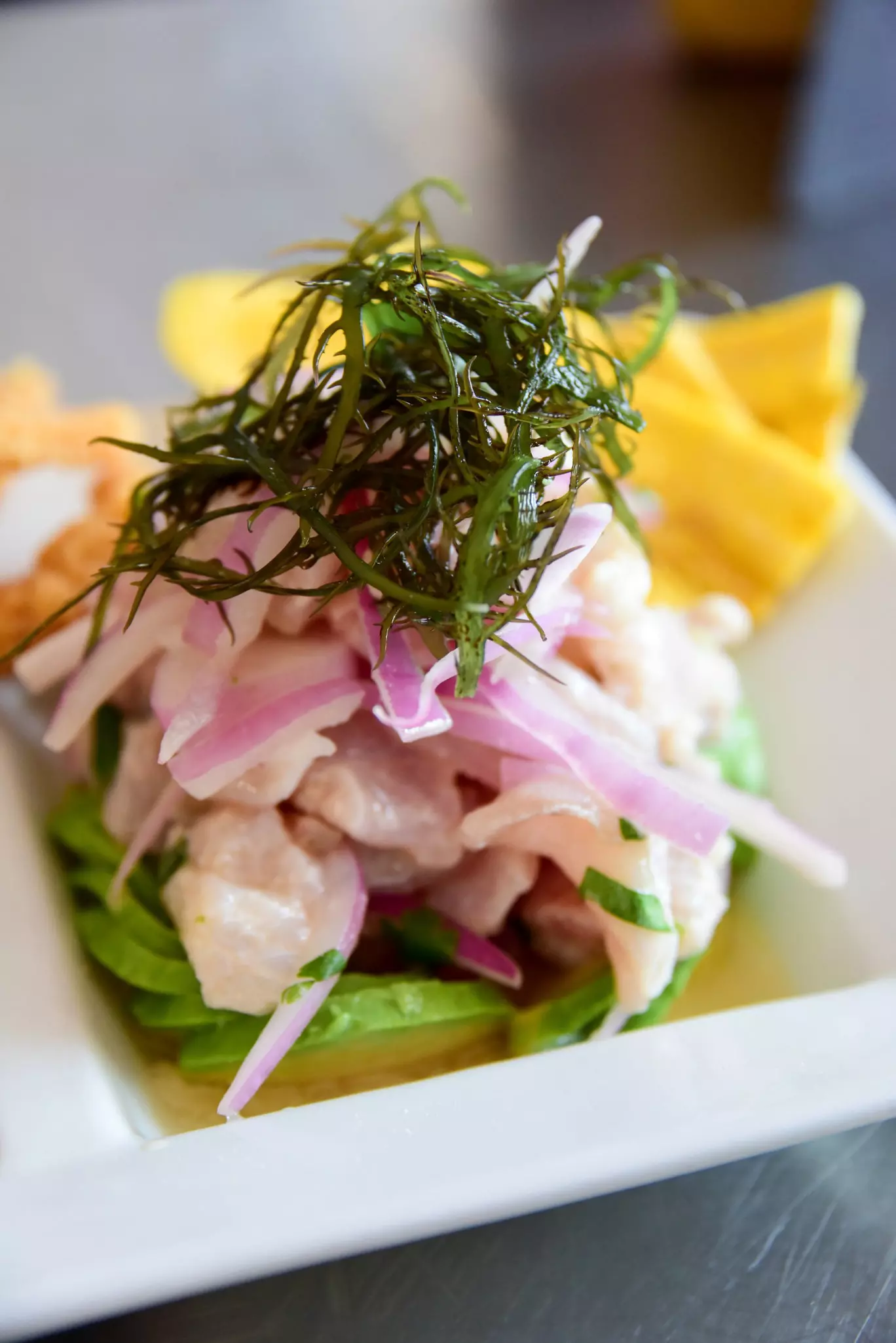 A close-in shot of a serving of ceviche, raw fish served with seaweed, plantain chips, cracklings and corn at a restaurant.