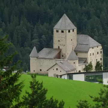Medieval Ciastel de Tor castle and its modern annex on a green hillside, home of the Museo Ladin in Val Badia