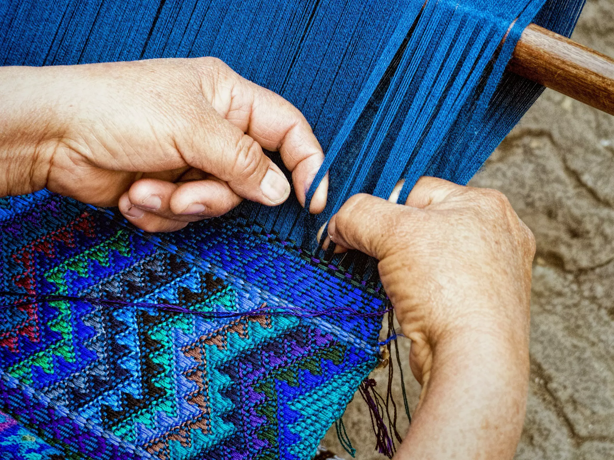 Two hands weave a pattern in bright blue thread in Guatemala.
