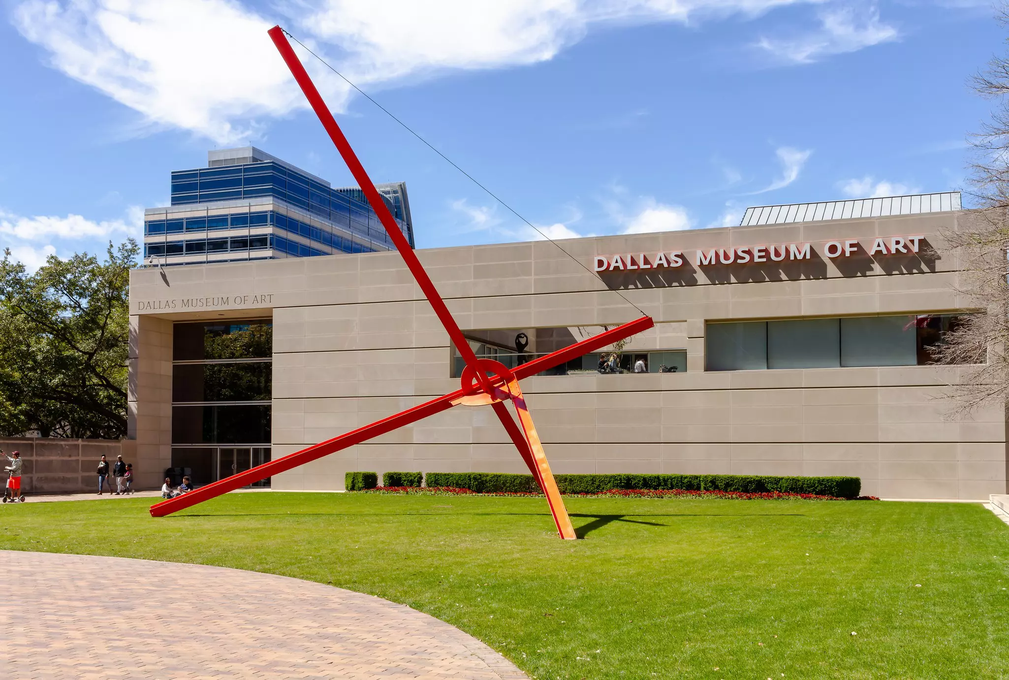 Exterior of a museum building with a large-scale sculpture comprising large red steel bars crossing over with a round intersection.