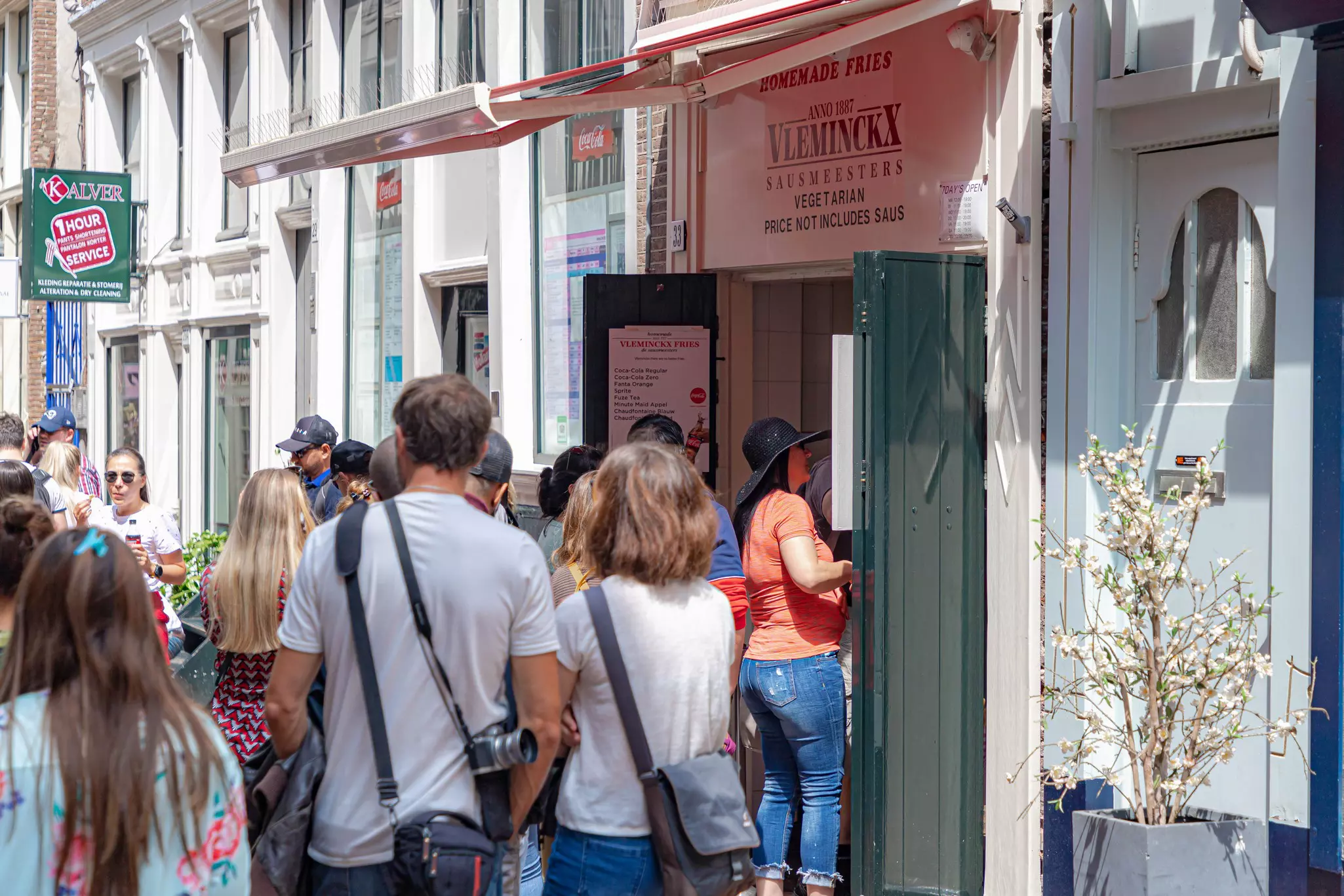 People line up at a doorway with a sign above it that says "Vleminckx Sausmeesters"