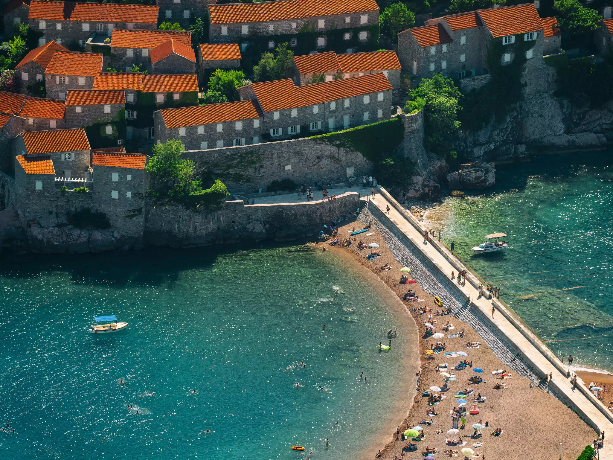 A view of stone buildings and a sea wall with a beach on one side and boats on the other