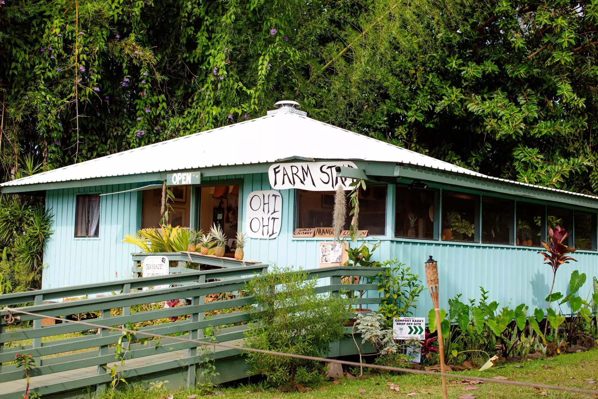Light blue wooden building with ramp leading up to it and hand-painted signs reading "Ohi Ohi" and "Farm Stand."