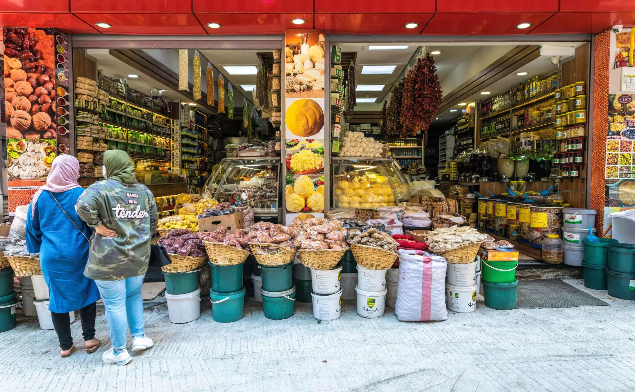 Two women stand facing a display of fresh produce at a small market shop in Trabzon, Turkey. 