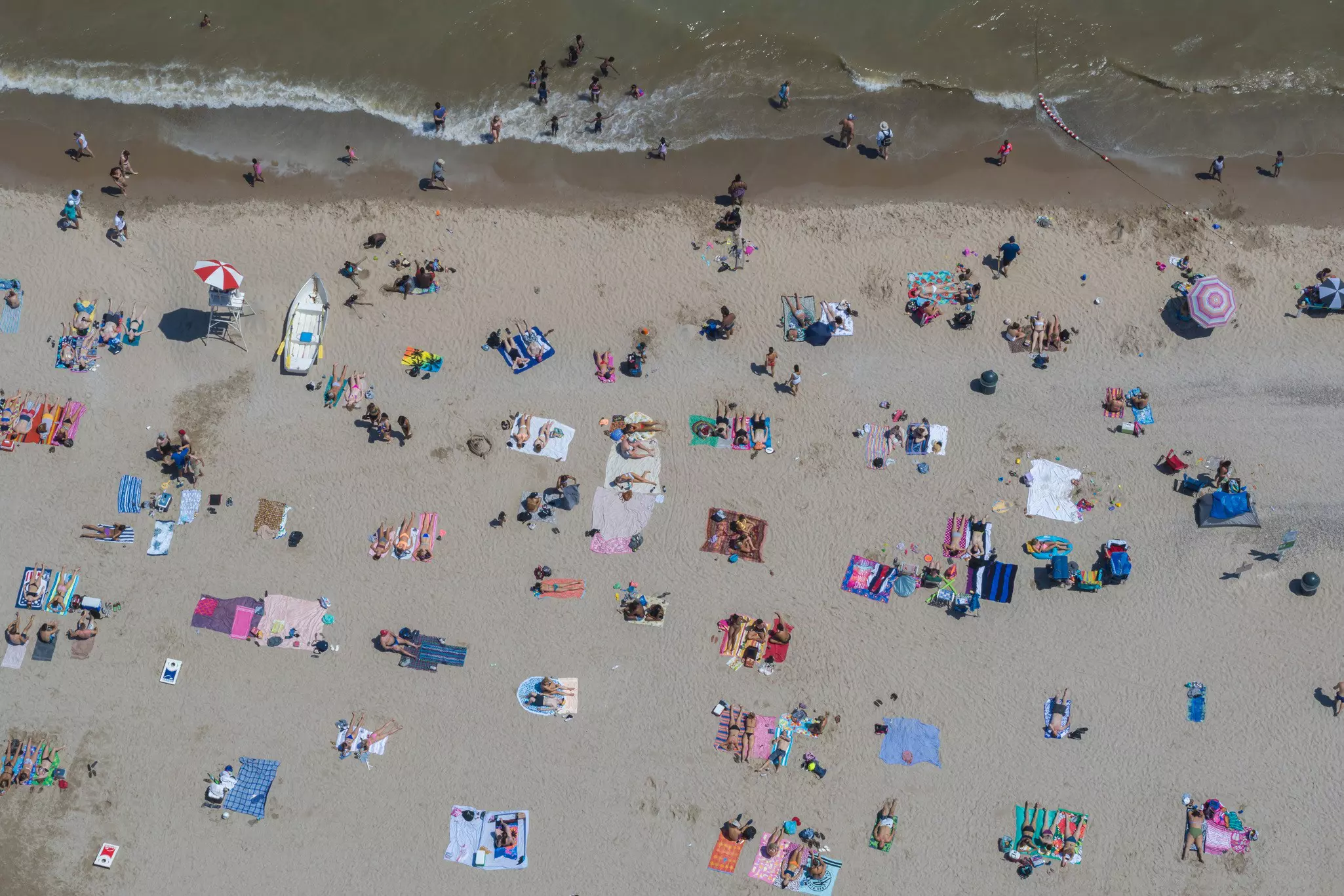 An overhead view of people sitting on towels and splashing in the water on a crowded beach.