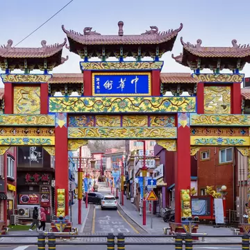 Red, gold and green Chinese-style gate with tiled roofs over a street lined with shops in Incheon Chinatown, South Korea.