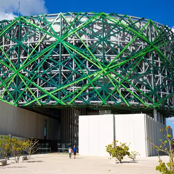 A round building topped by an intricate lattice of green and white steel beams.