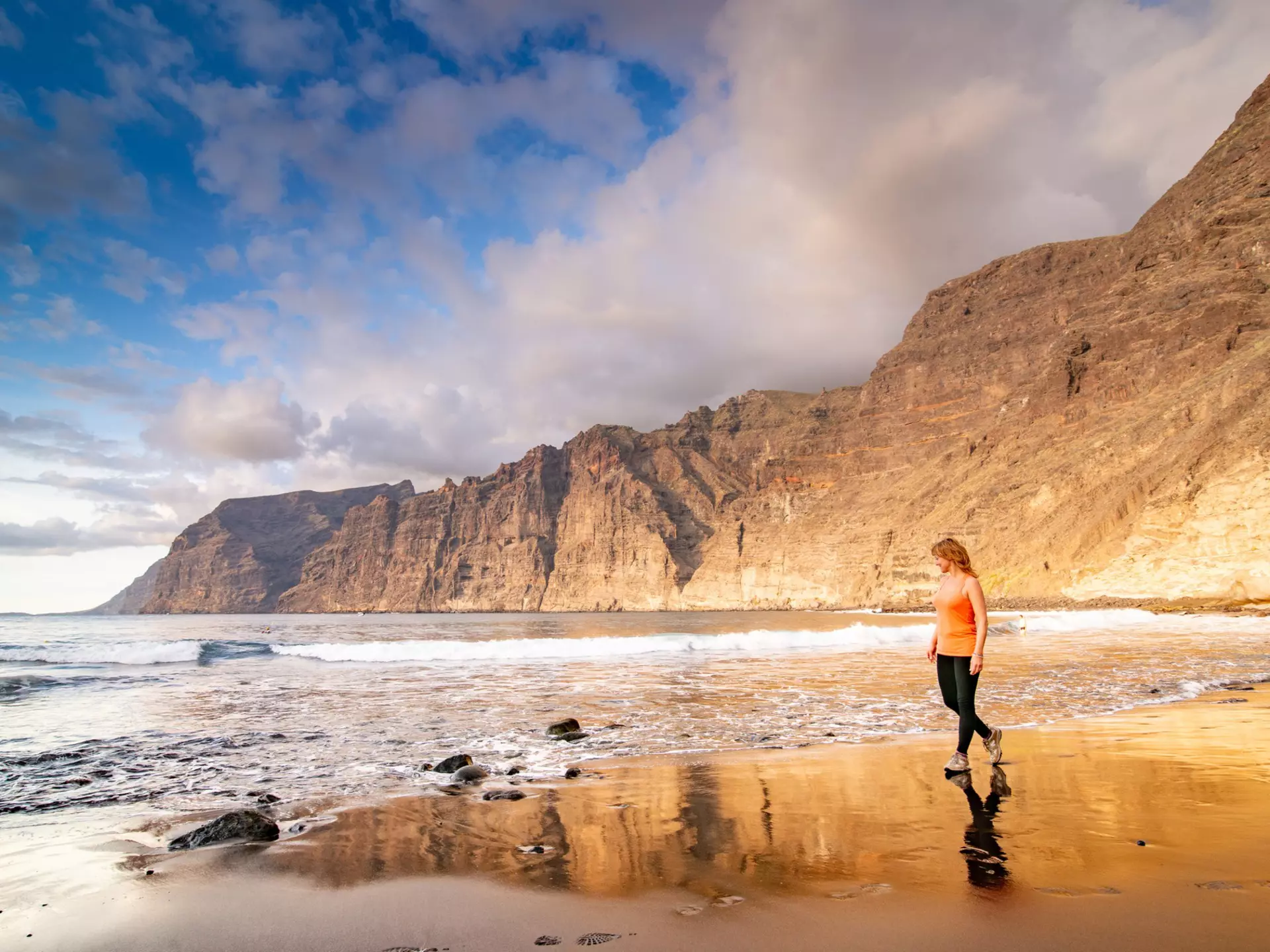 Adult woman walking along the beach in Tenerife, backed by huge sheer rocky cliffs