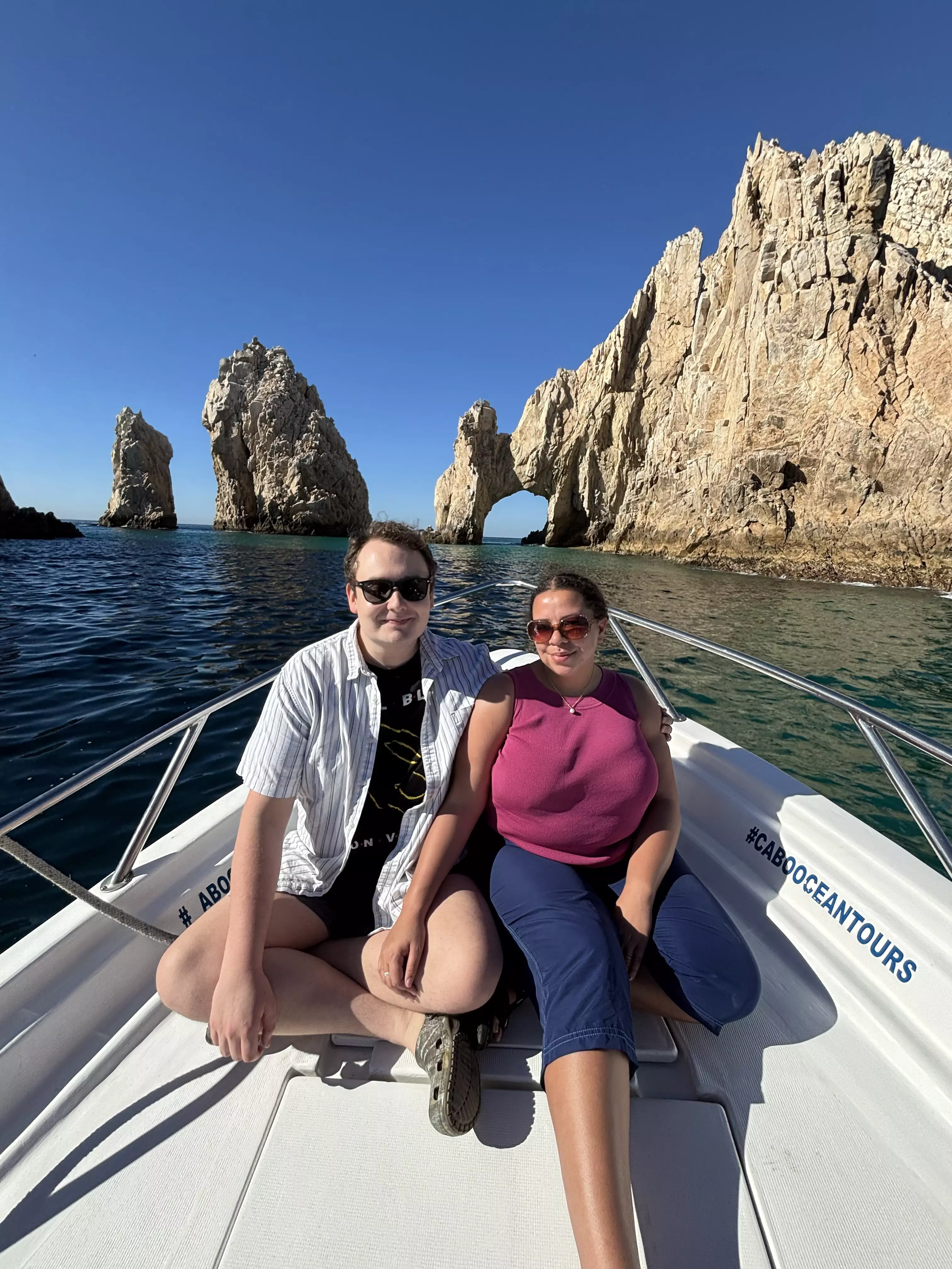 Two people in a boat with a natural stone arch in the background.