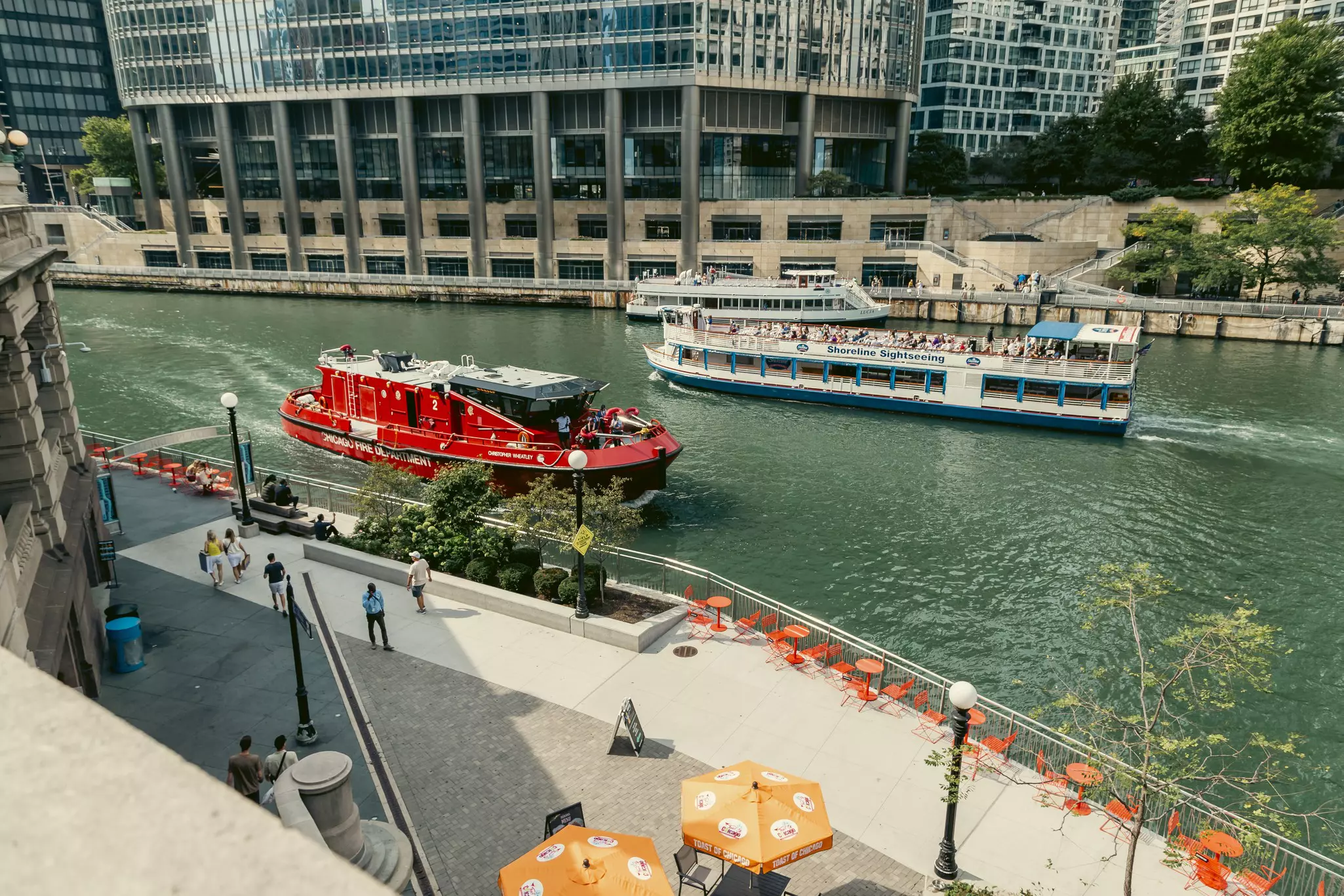 A red river boat passes a tour boat in a high-rise city.