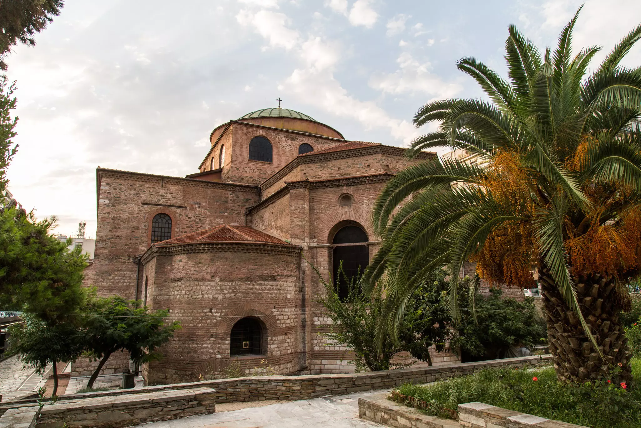 A brown building with a cross on top of its dome. Palm trees are in the foreground.