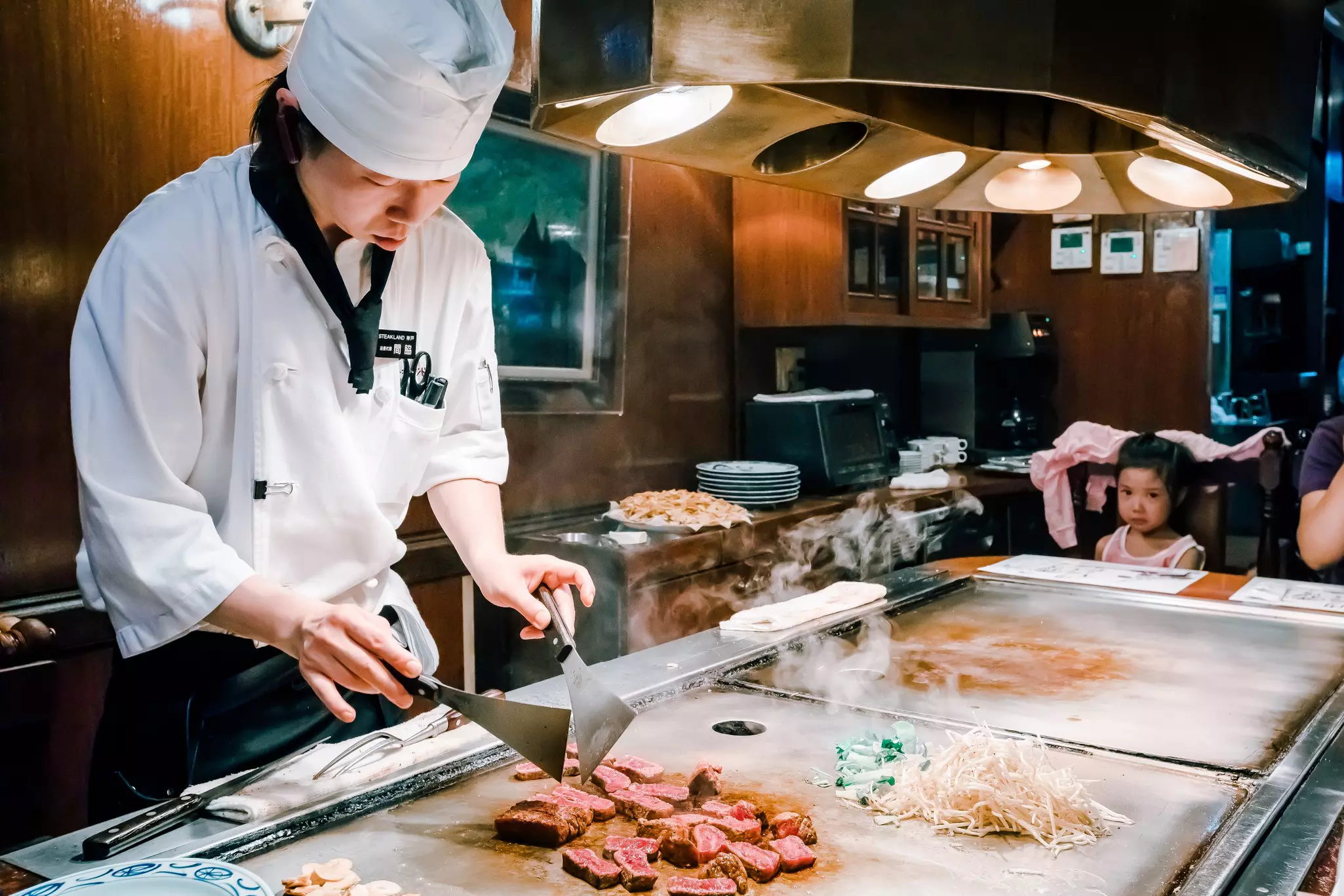 A chef slicing red meat on a flattop cooking surface.