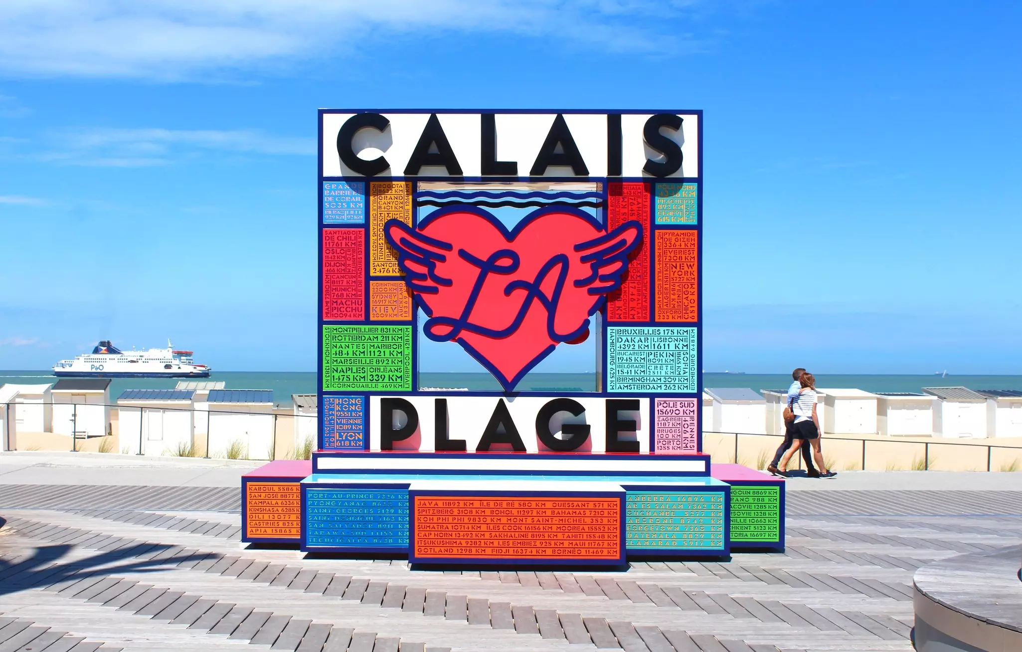 A large colorful sign forms an art installation on the waterfront near the beach