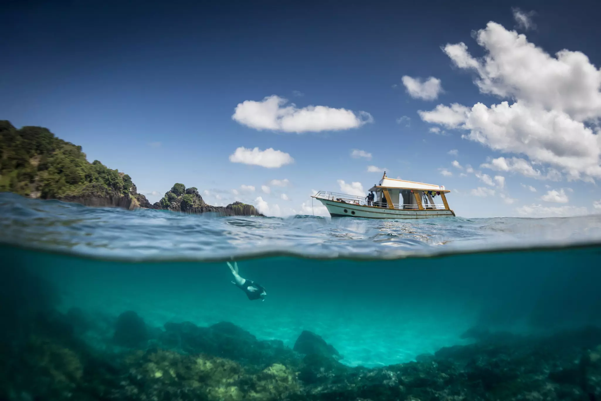A boat and a woman free diving at Sancho beach in the archipelago of Fernando de Noronha, Brazil.