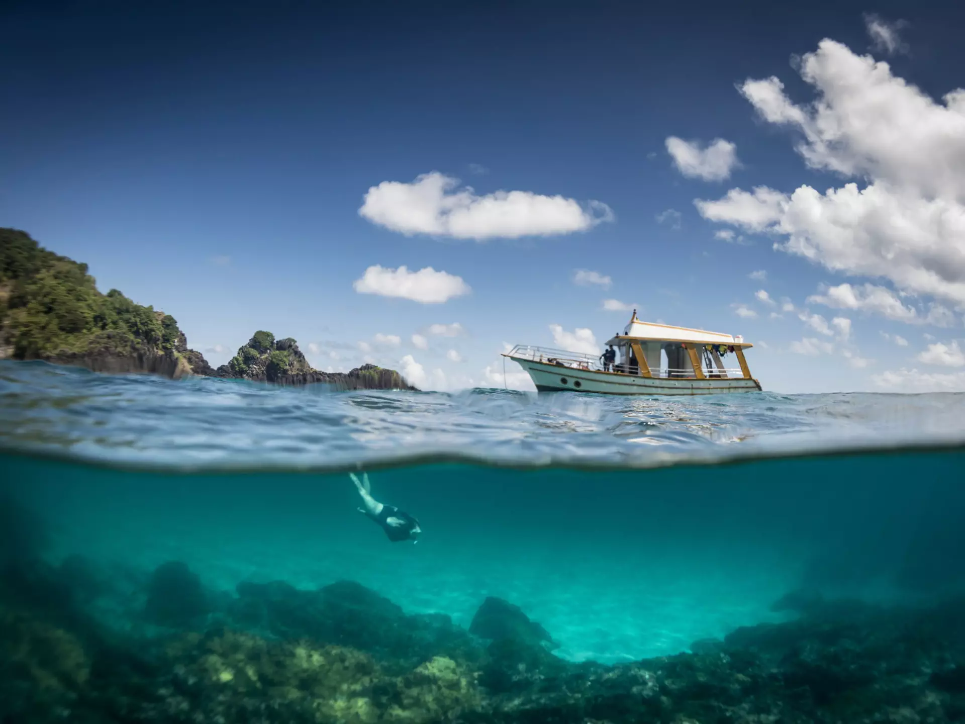 A woman snorkels underwater while a small tour boat moors nearby
