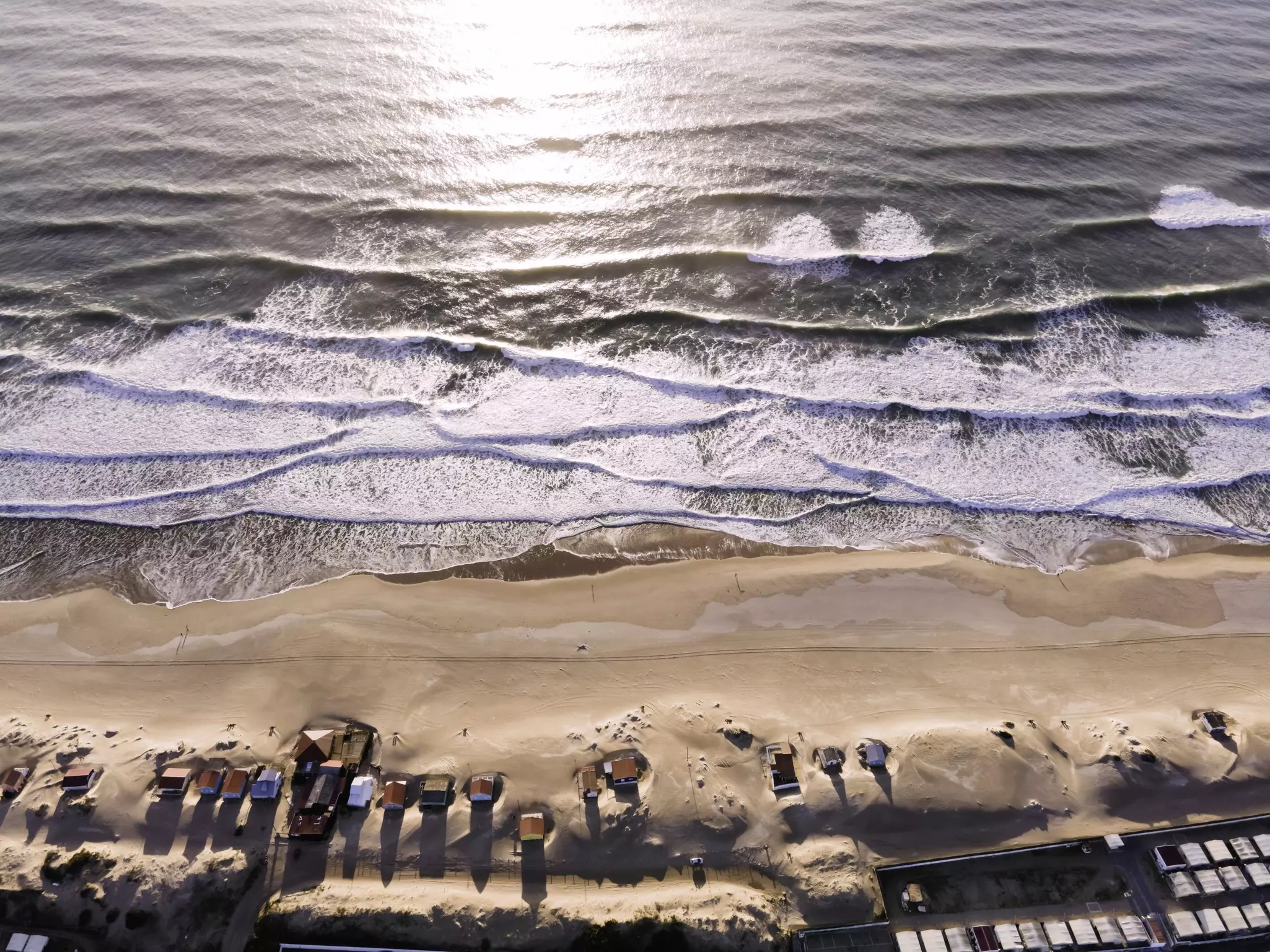Beautiful aerial view of the small village along the beach at Costa da Caparica near Lisbon downtown. Drone view of the waves crushing on the paradise portuguese beach at sunset on a beautiful location.