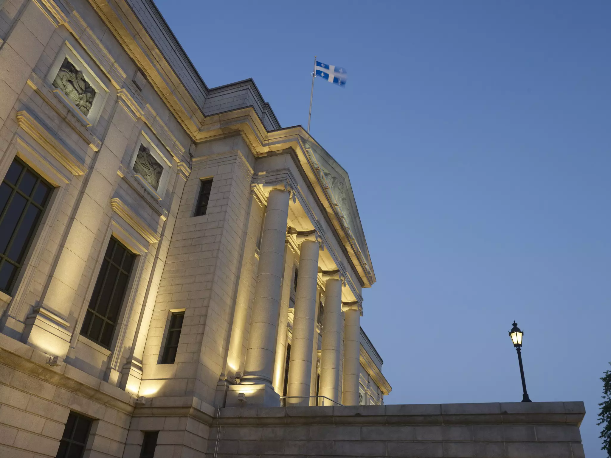 Exterior of a white stone museum with columns out front and a lighted lamppost in early evening.