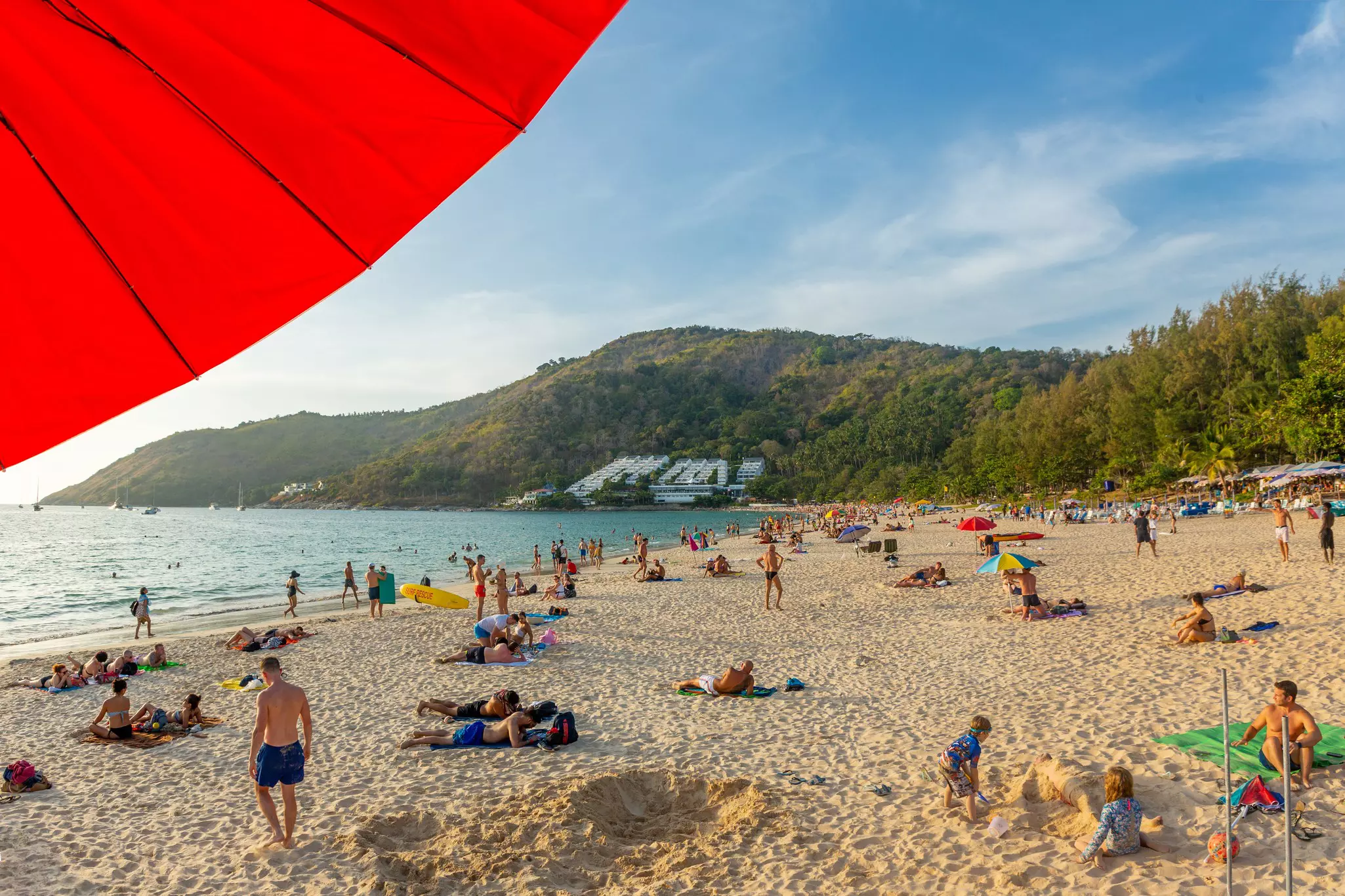 A beach scattered with people with verdant hills in the background