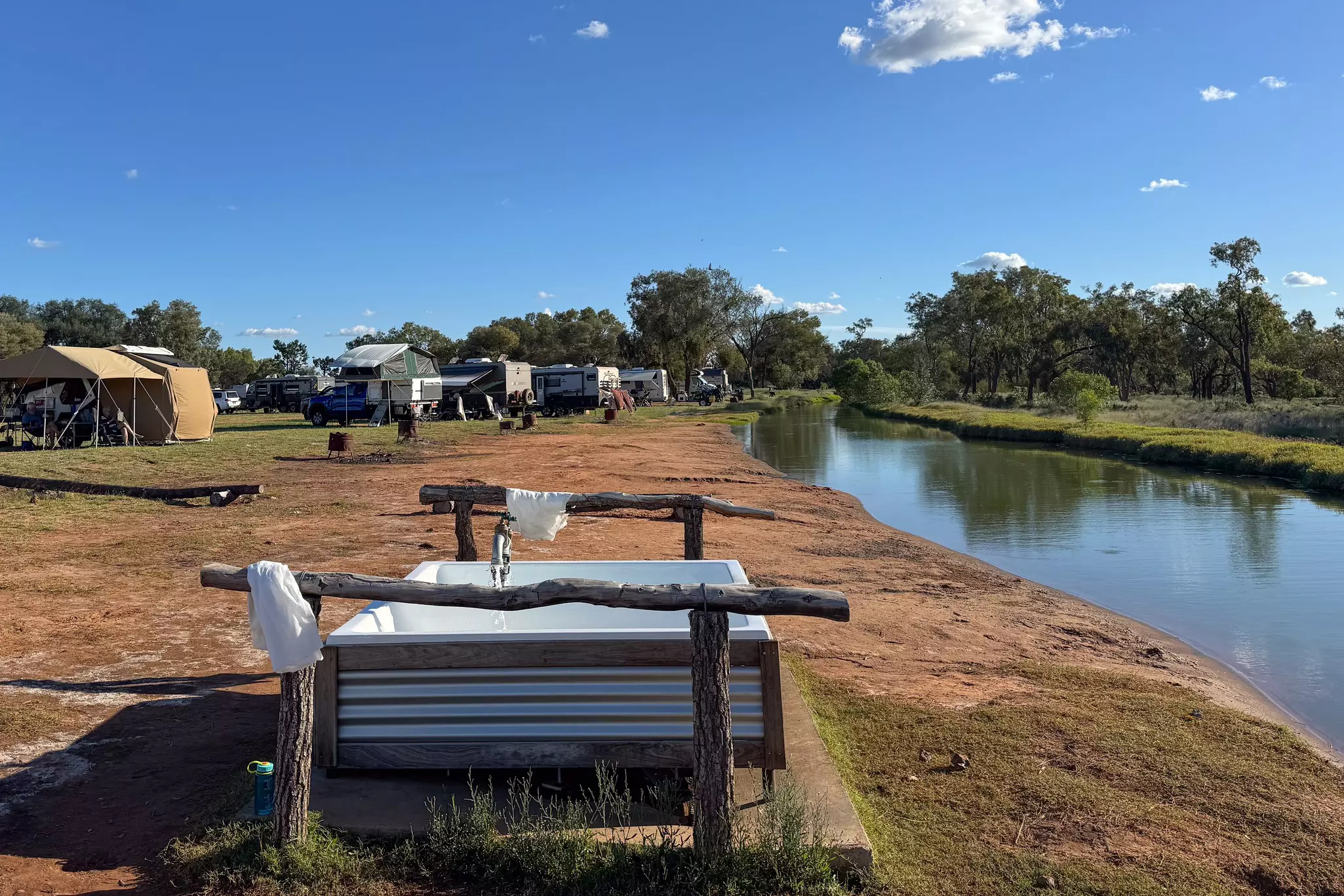 A riverside hot-spring tub at the edge of a campground with tents and RVs.