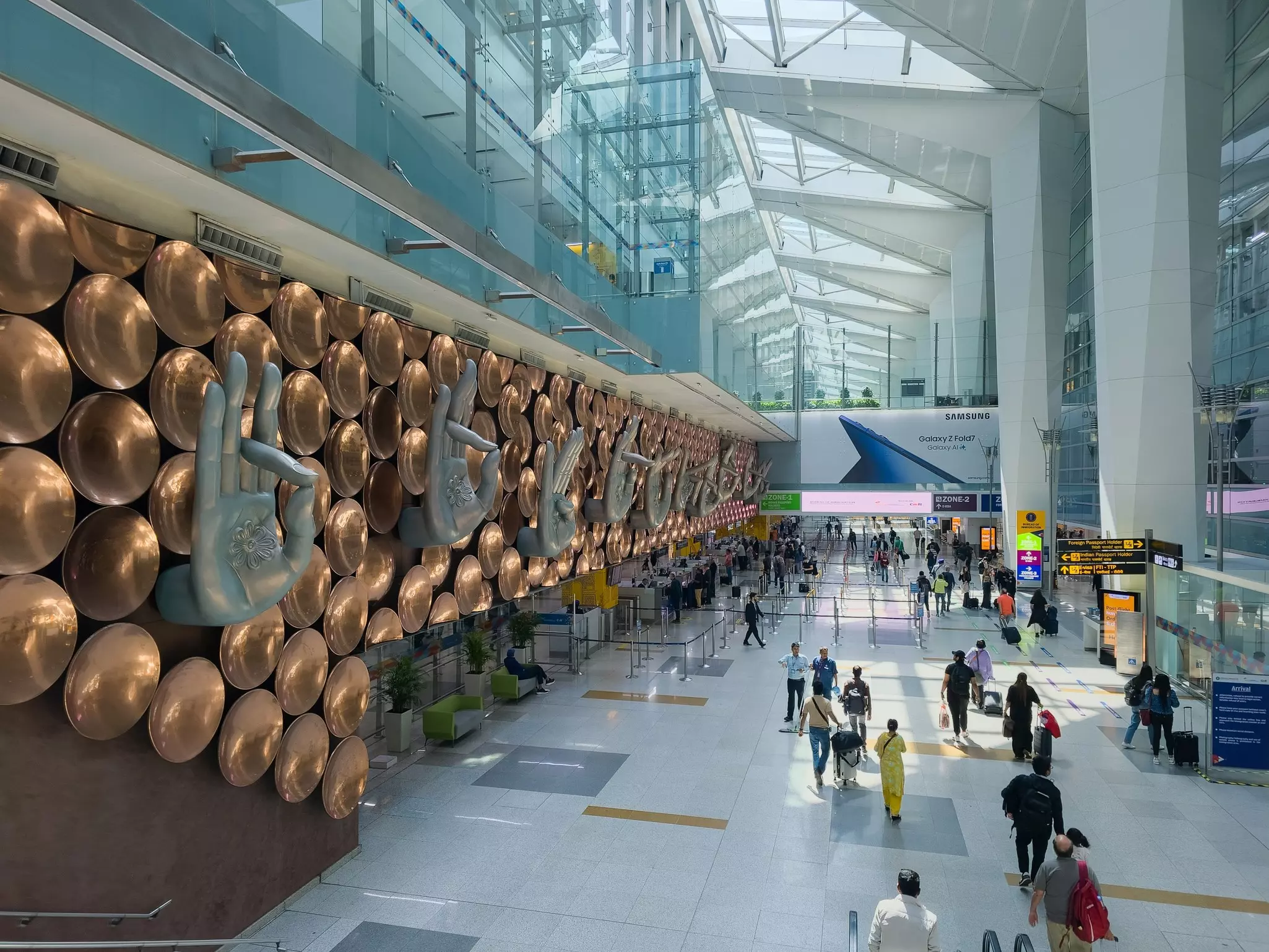 Passengers walking in the sun-lit arrival hall inside Indira Gandhi International Airport, Delhi, India.