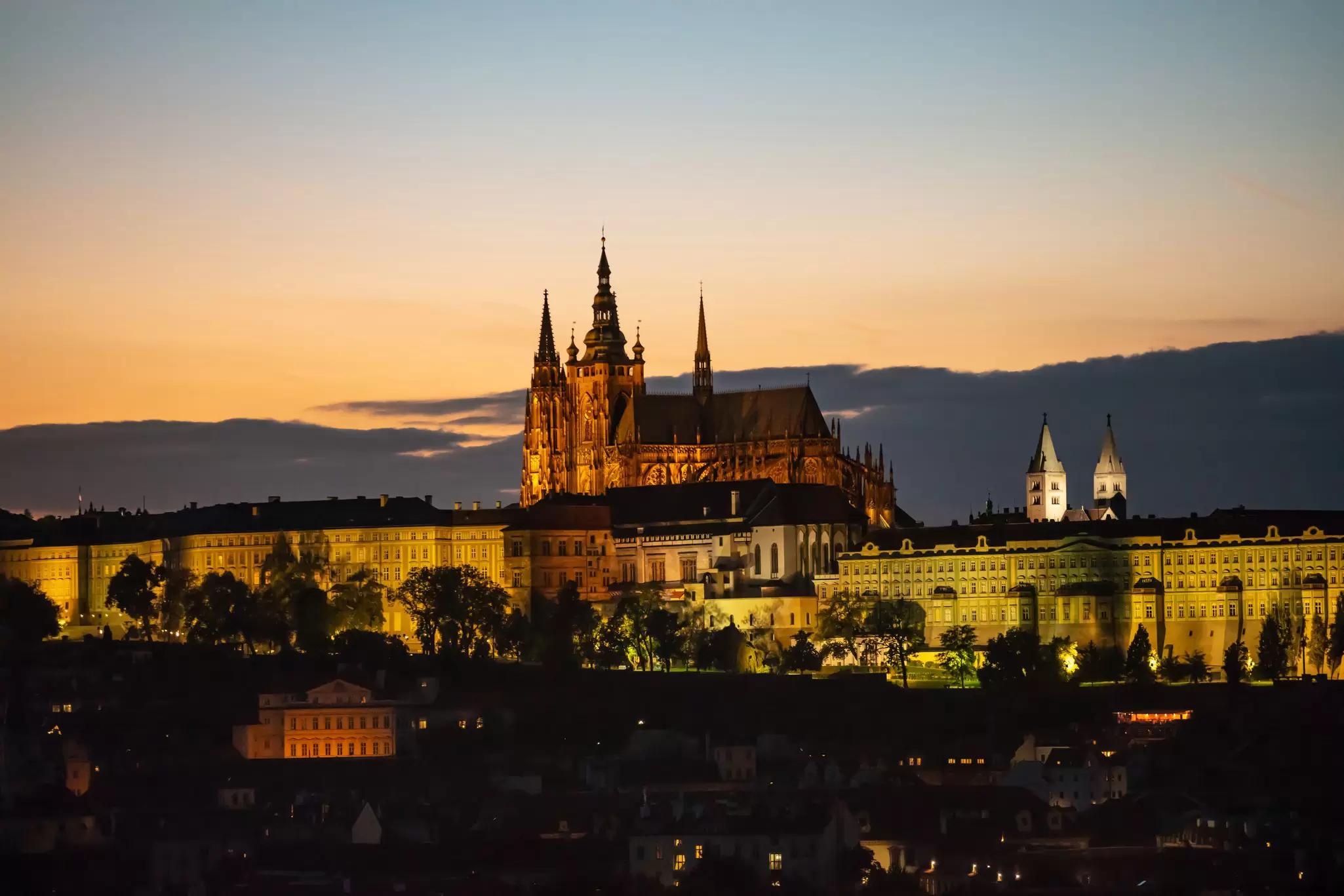 View of the illuminated Prague Castle and St. Vitus Cathedral during sunset in Czechia.