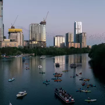 Aerial view of boats and kayaks on the water during sunset, as bats fly in the air in Austin, Texas.