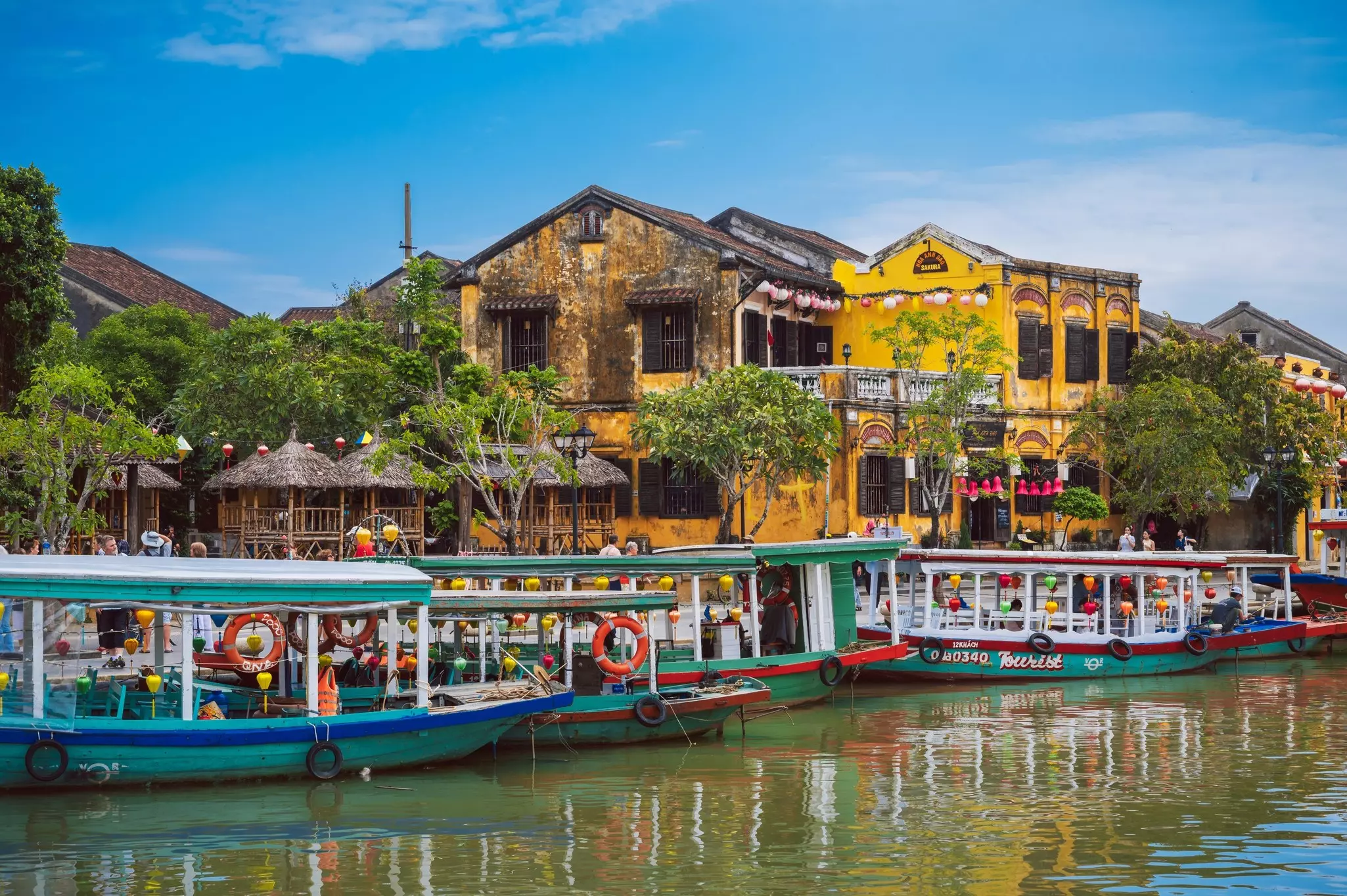 Colorful boats docked near hut-like structures and a large, weathered yellow building