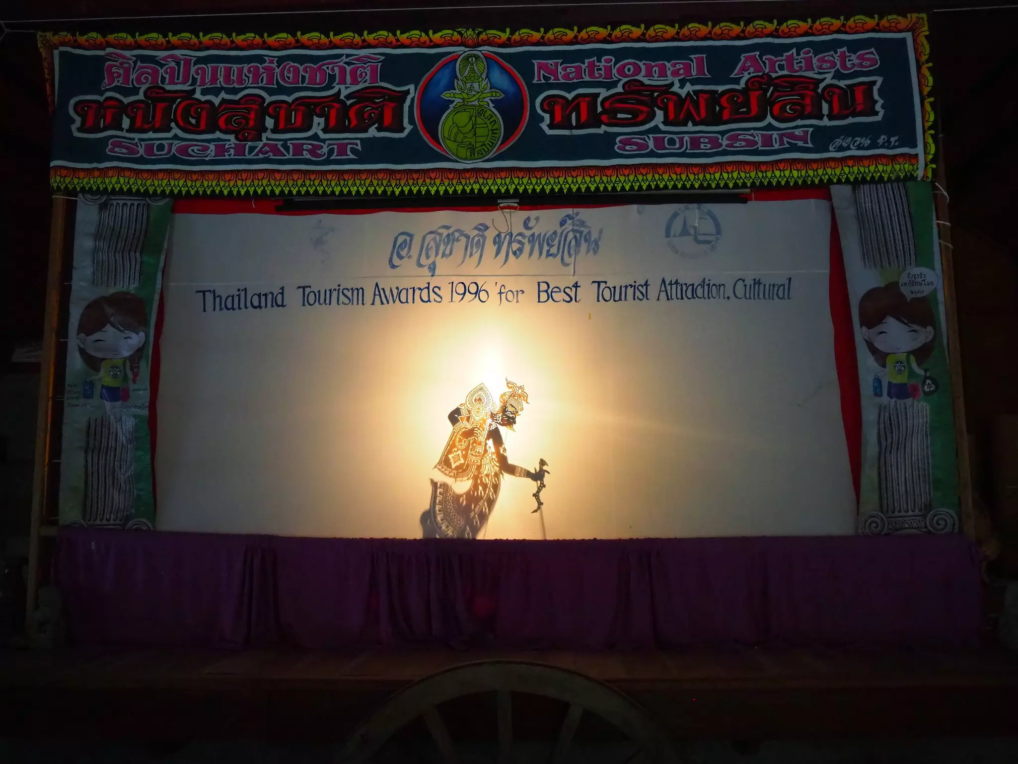 A shadow puppet illuminated on a white screen in a darkened theater