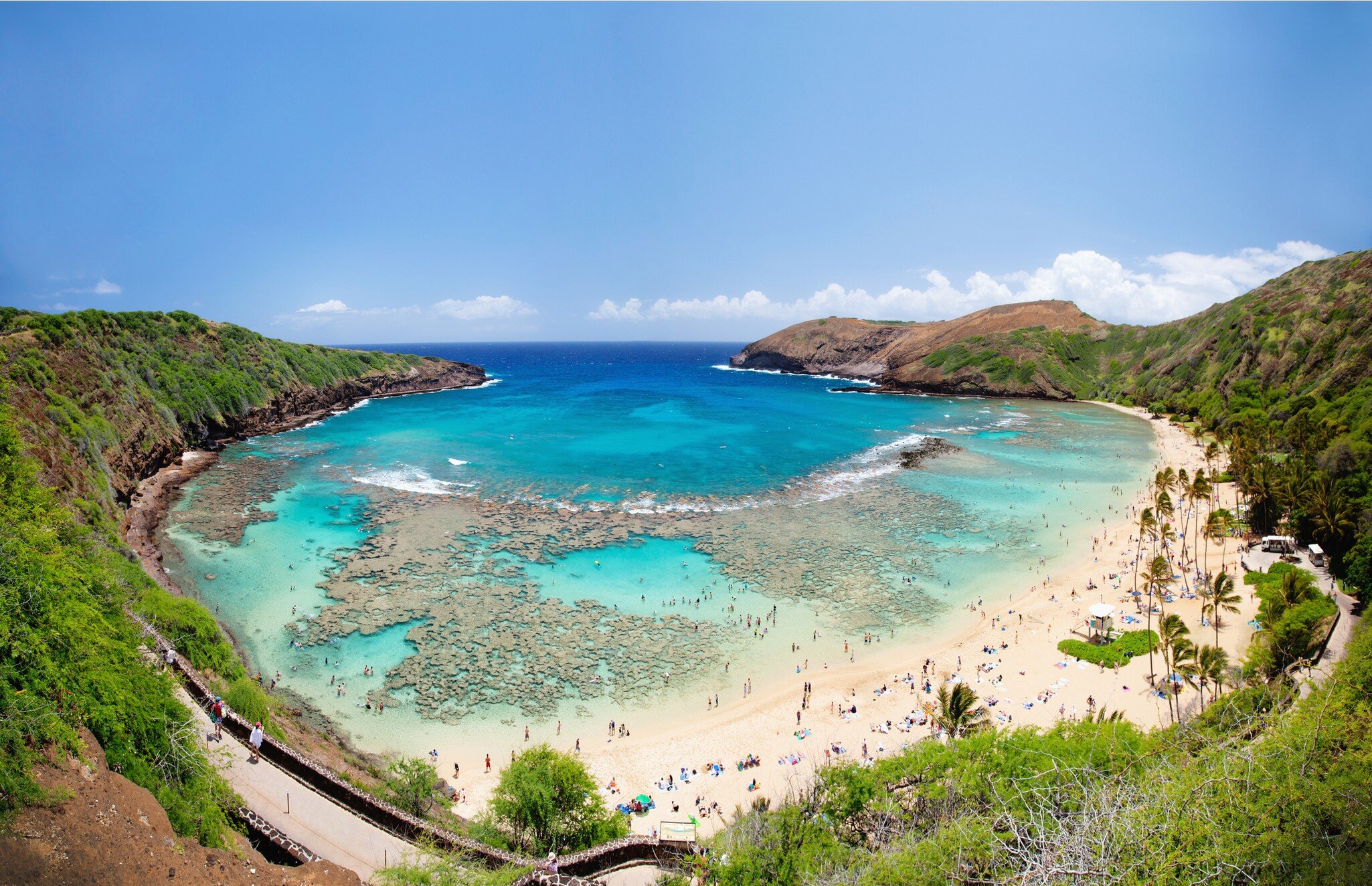People head out into the turquoise waters of a large cove with shallow reefs