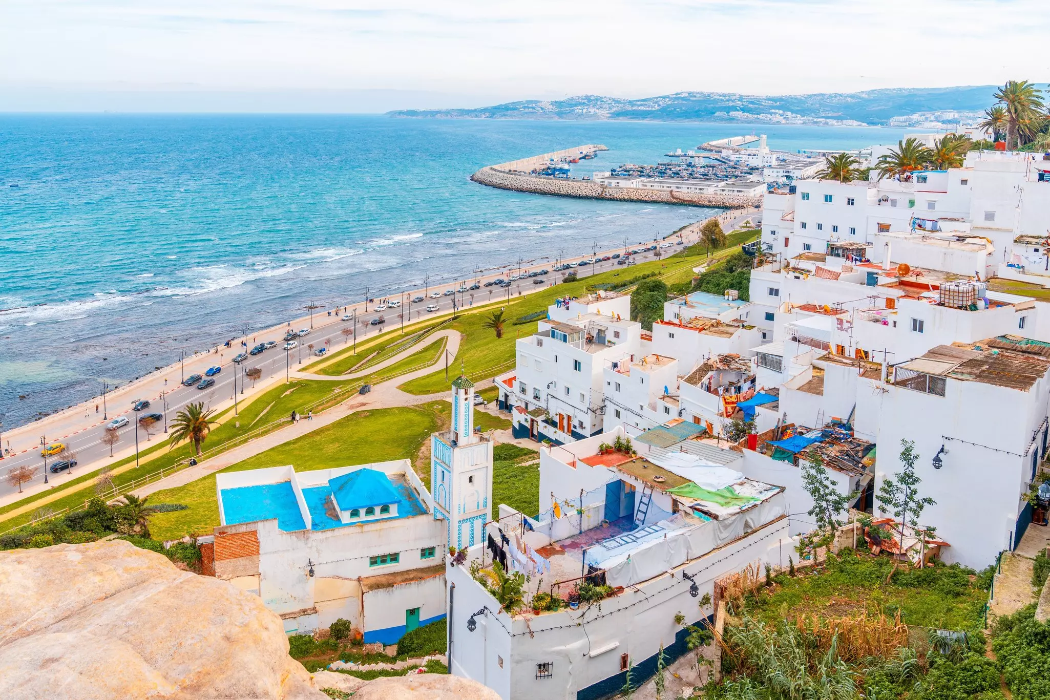 White buildings with colorful roofs along a paved road that hugs a blue-watered coast