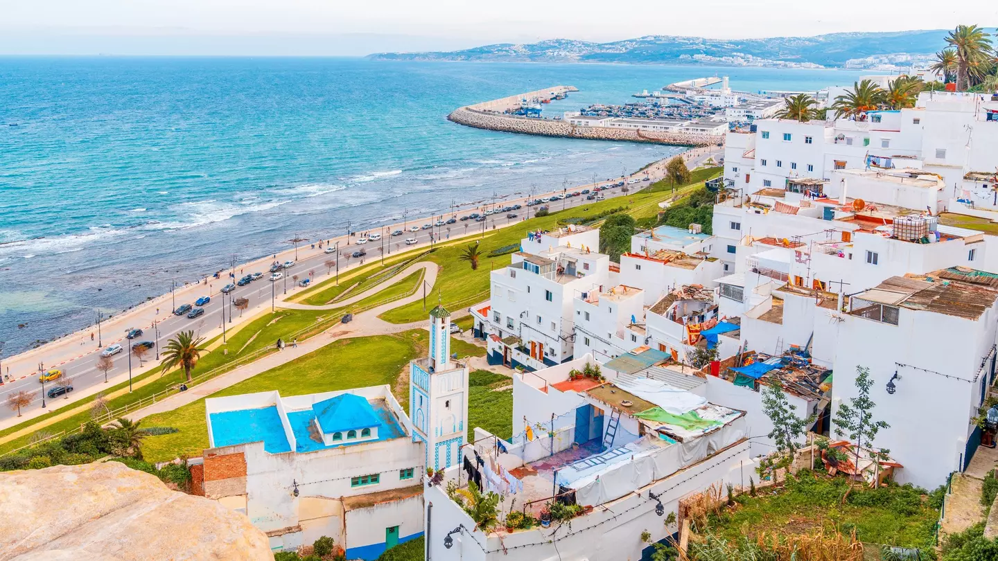 White buildings with colorful roofs along a paved road that hugs a blue-watered coast