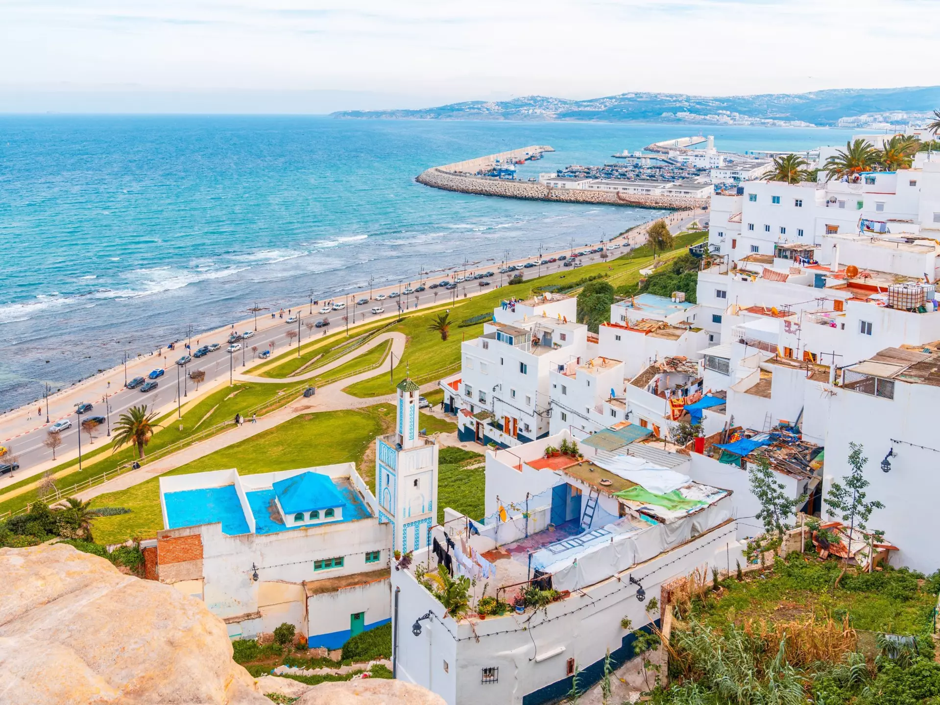 White buildings with colorful roofs along a paved road that hugs a blue-watered coast