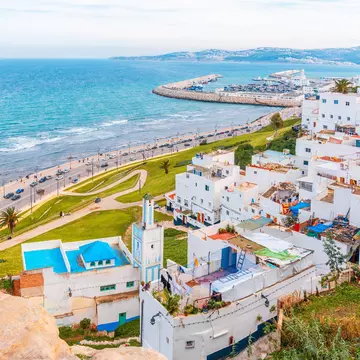White buildings with colorful roofs along a paved road that hugs a blue-watered coast