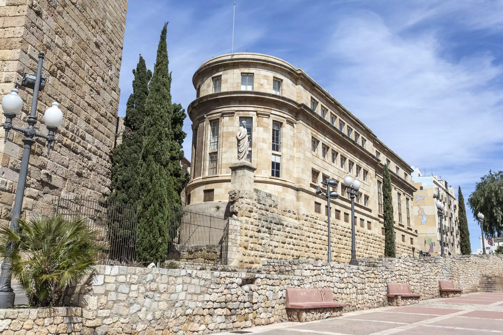Exterior of a large stone museum building beside a path with benches below it.