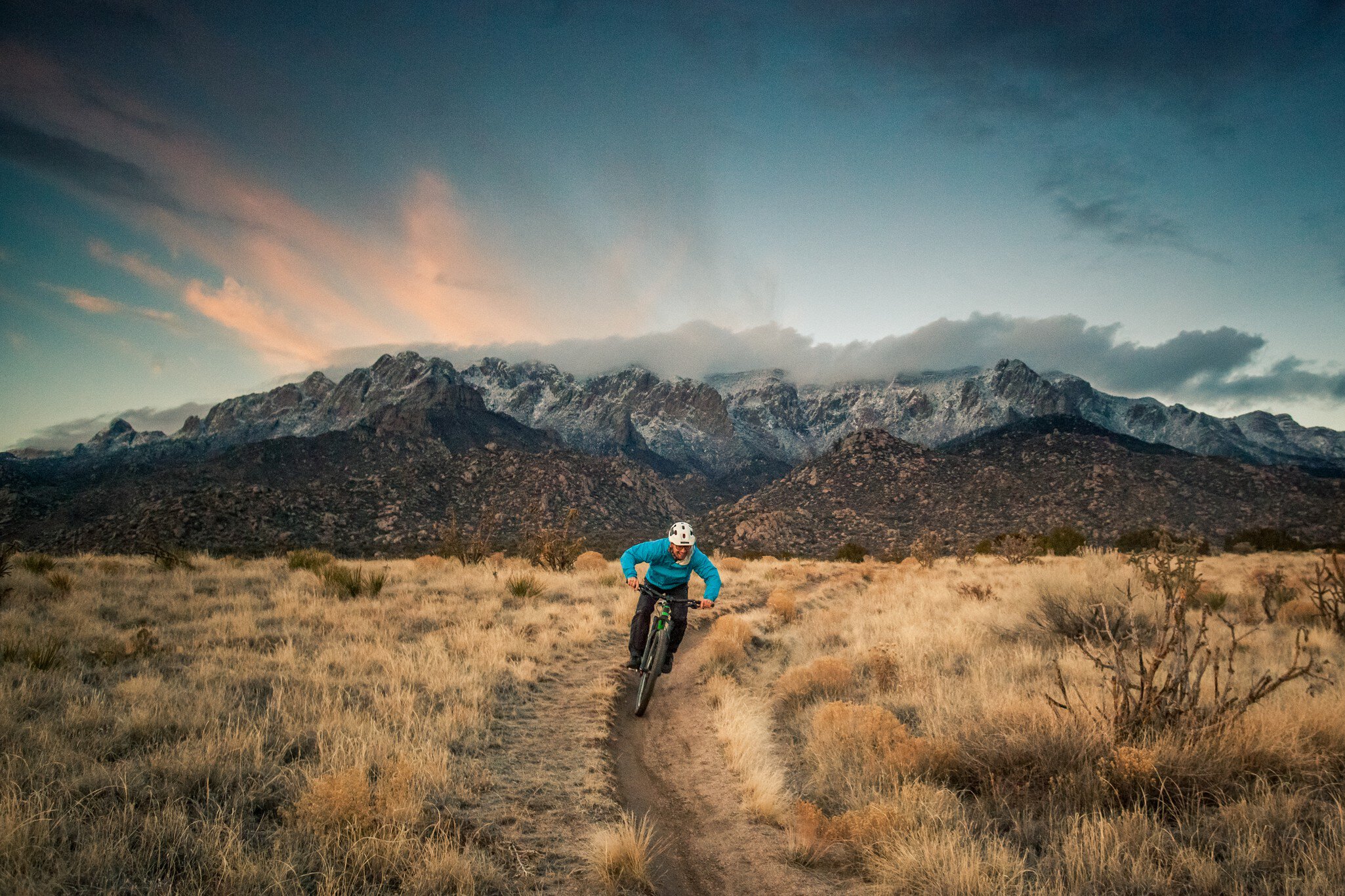 happy and joyful smiling mountain biking man descending desert mountain terrain in the cool blue hues of dusk.  wide angle horizontal composition.  sandia mountains.  albuquerque, new mexico.