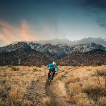 happy and joyful smiling mountain biking man descending desert mountain terrain in the cool blue hues of dusk.  wide angle horizontal composition.  sandia mountains.  albuquerque, new mexico.