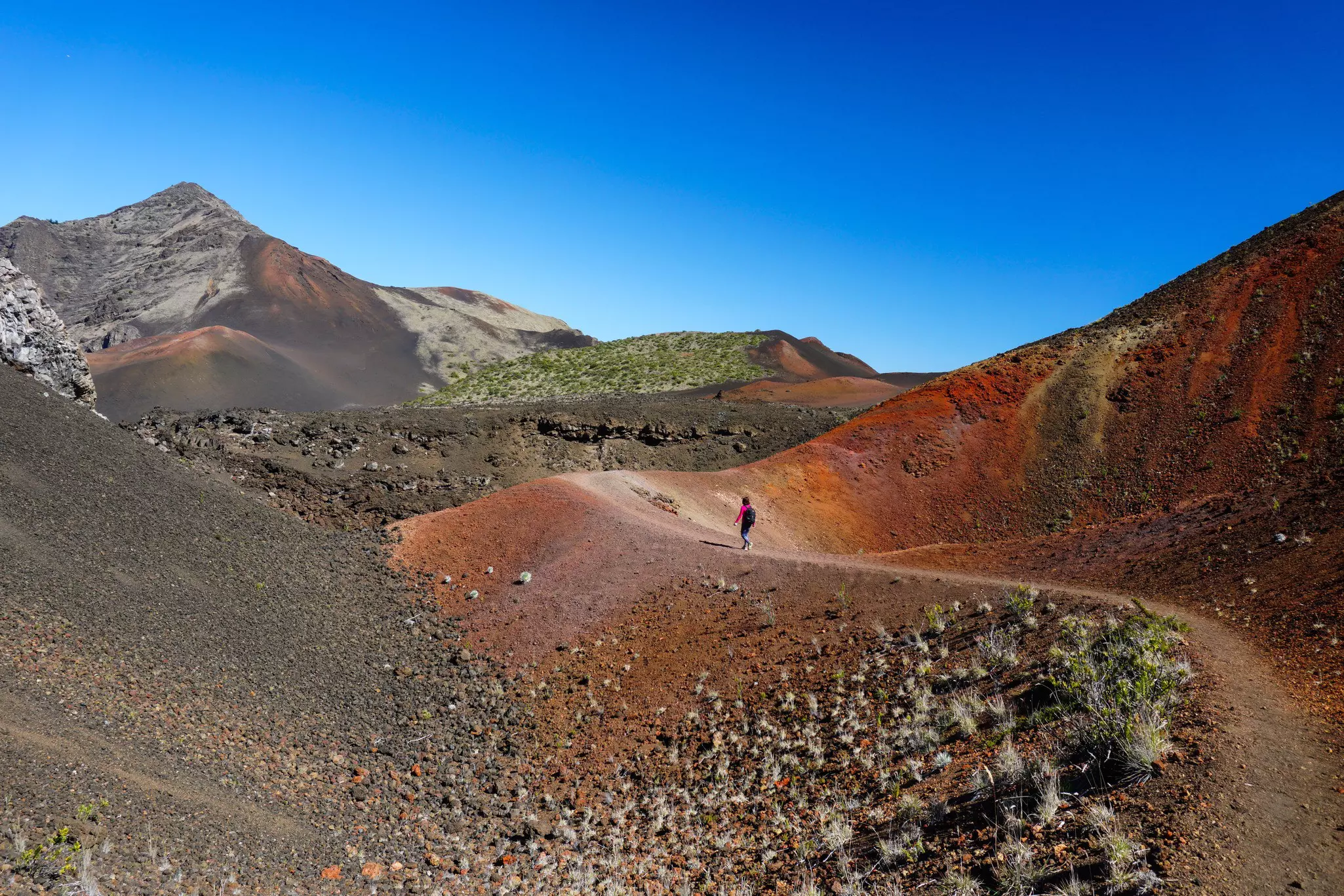 A single hiker on a reddish dirt trail in Haleakalā National Park in Oʻahu