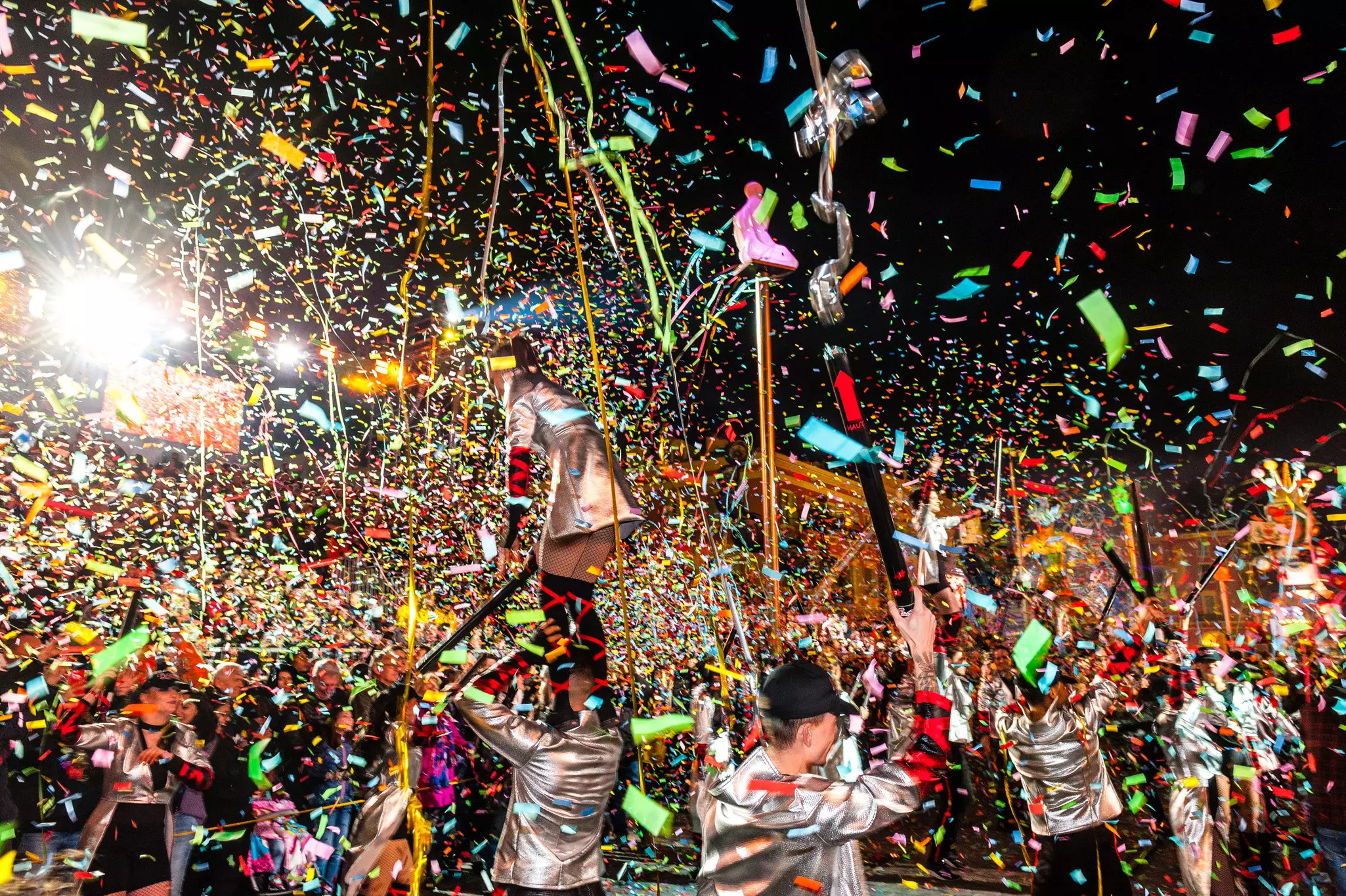 Confetti fills the air during an evening parade and street party in a city.