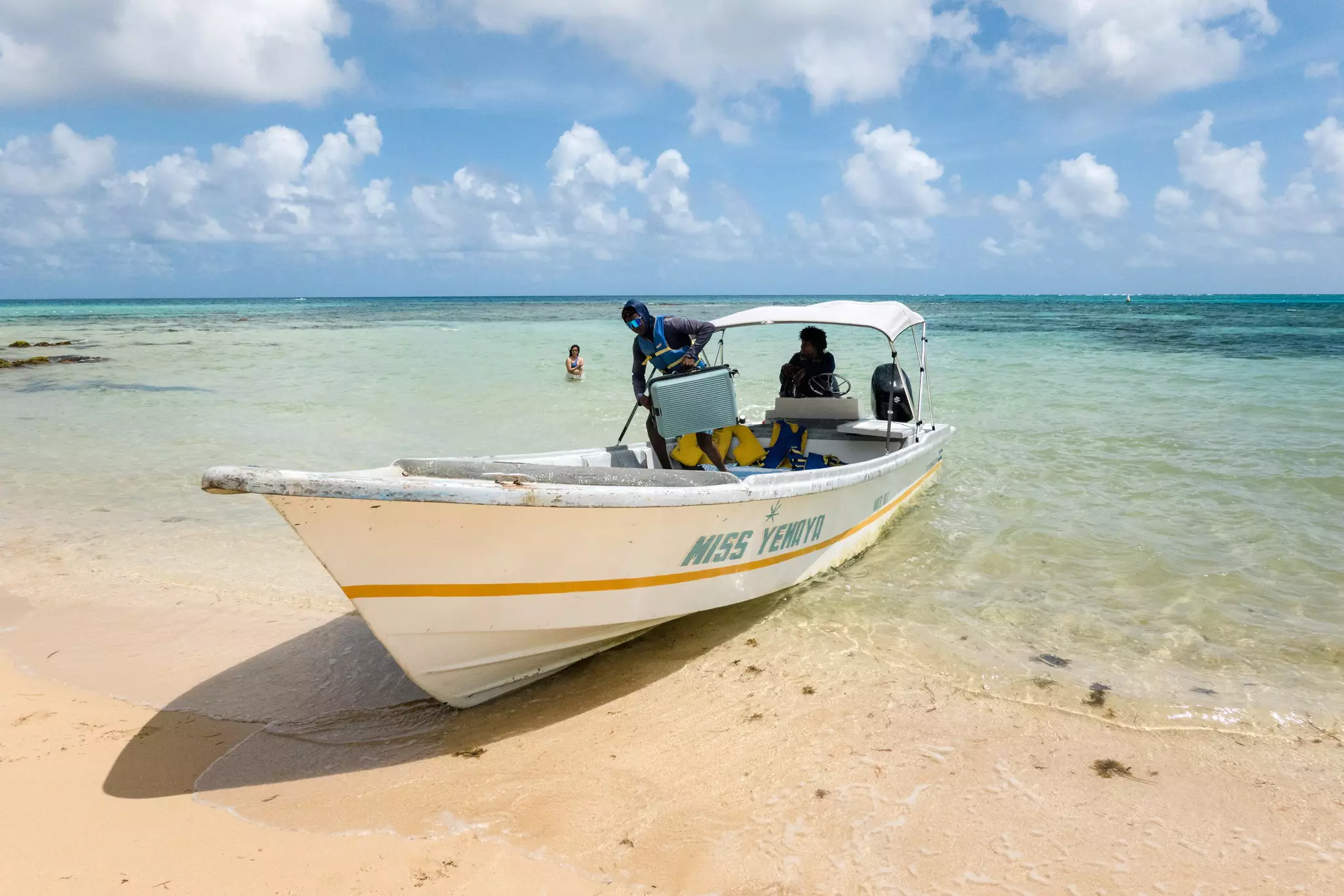 A small boat docks on a sandy beach. A person lifts a suitcase as they prepare to disembark.