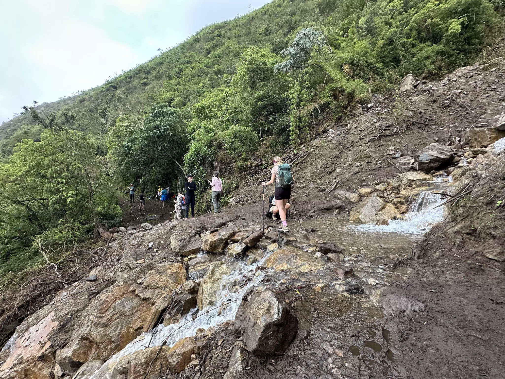 People passing over a water crossing on a muddy, rocky trail