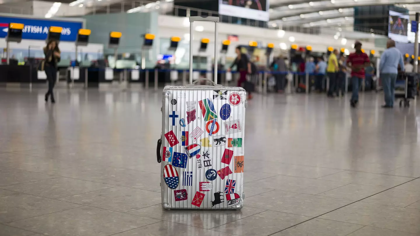 A suitcase full of stickers of various countries sits in an airport departure area. $125 travel ideas
