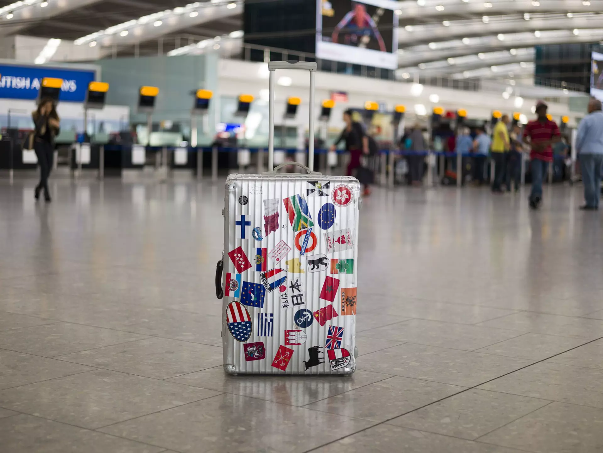 A suitcase full of stickers of various countries sits in an airport departure area. $125 travel ideas