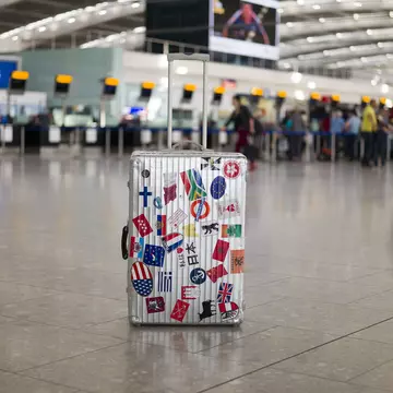 A suitcase full of stickers of various countries sits in an airport departure area. $125 travel ideas