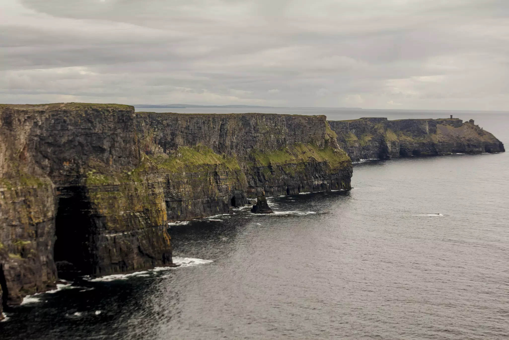 Large, flat sea cliffs jutting out into a dark ocean on an overcast day.