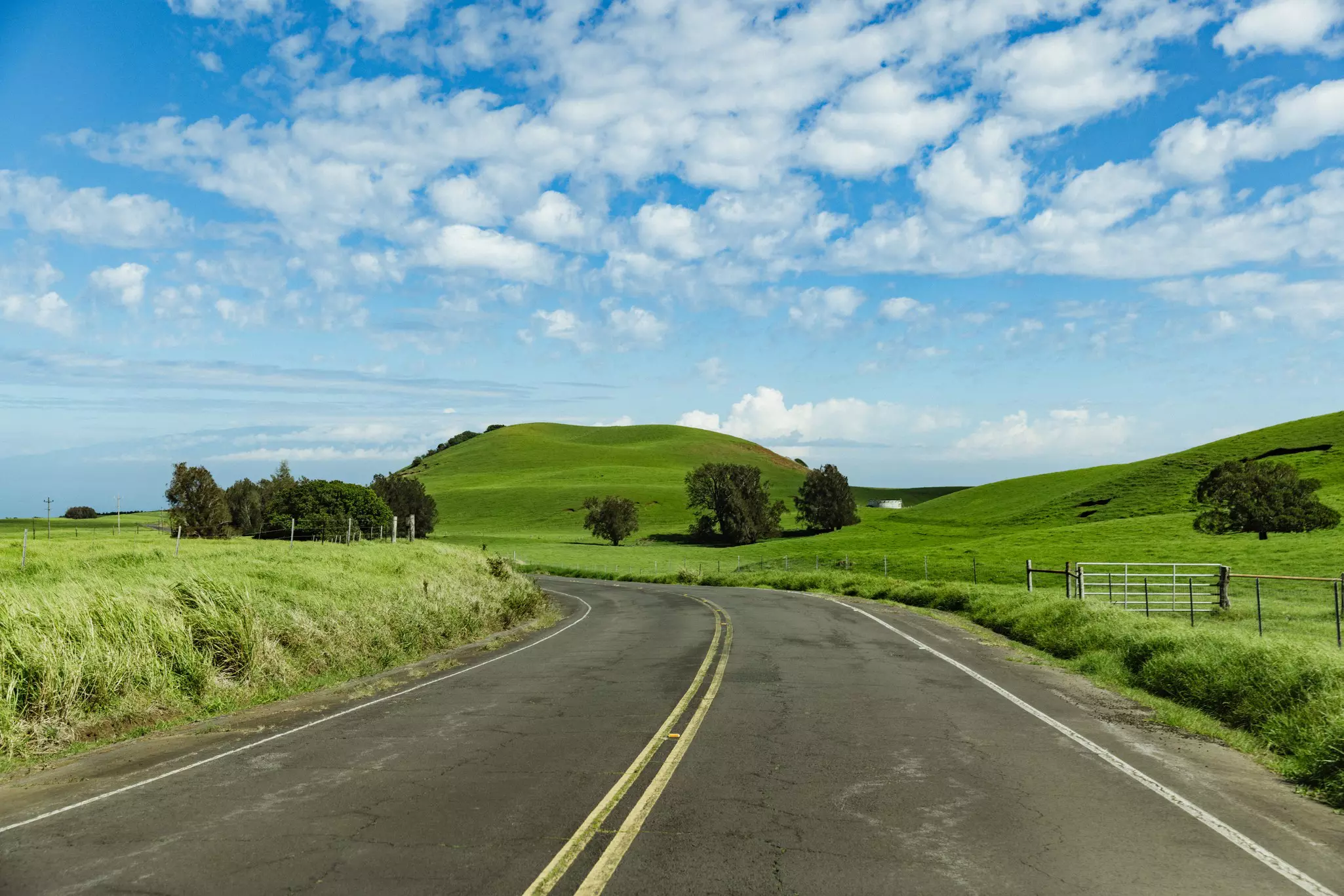 A two-lane blacktop road with a large green hill ahead.